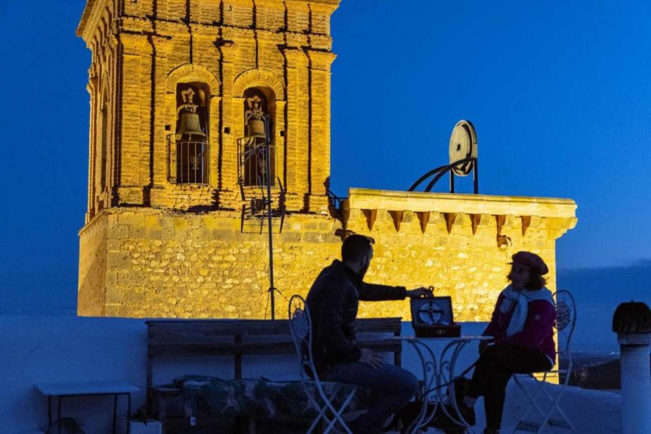 La Casa del Cine en Níjar at dusk, with the illuminated bell tower of the village church above the rooftop terrace
