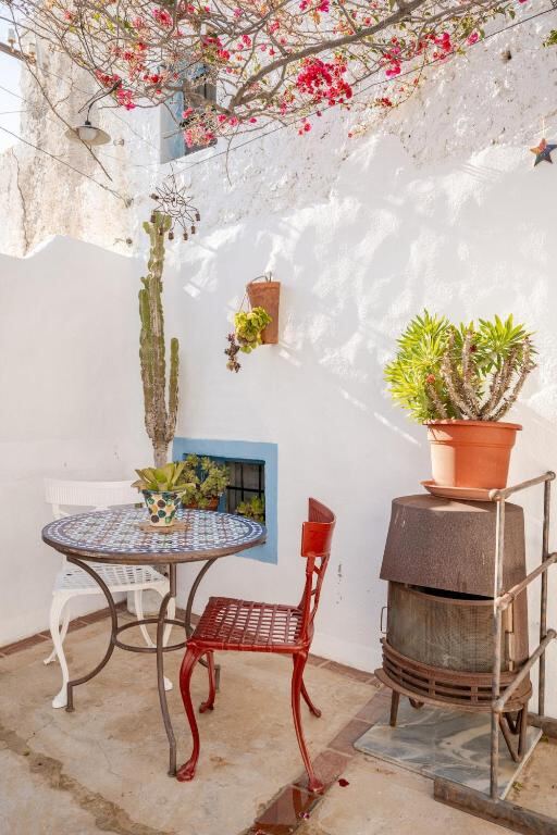 Corner of the patio with a tiled table, red chair and potted cactus against a white wall