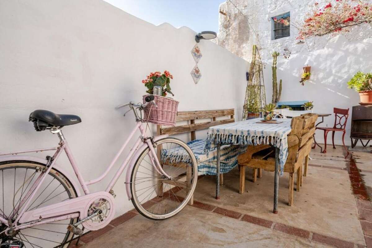 Bicycle leaning against a whitewashed wall beside a long table set for lunch on the patio